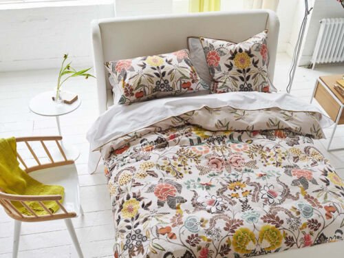 Bett mit Bettwäsche mit opulentem Blumenmuster in Rot, Gelb und Grün auf sandfarbenem Fond