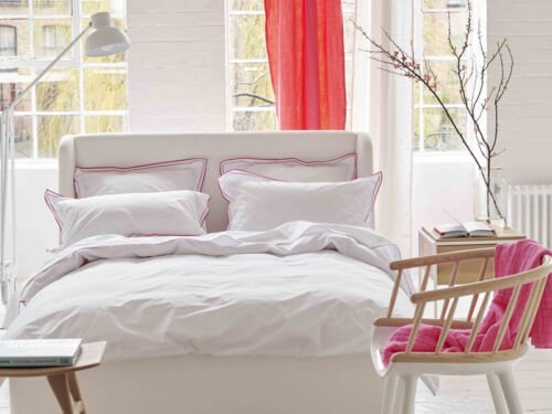 Bett mit weißer Bettwäsche mit pinkfarbenen Ziernähten